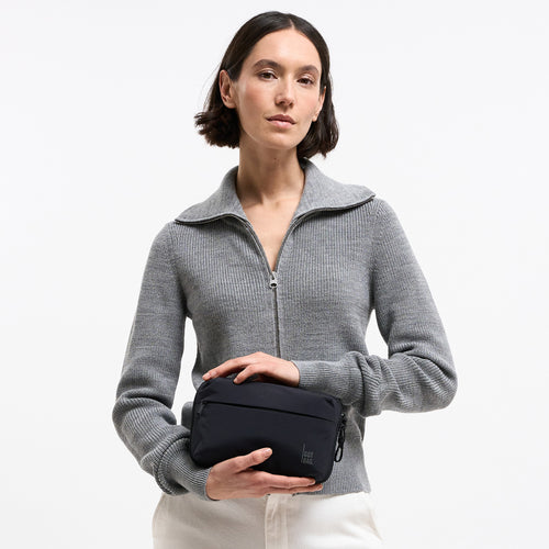 COMMUTER TECH POUCH Tasche in black (Schwarz) von einer Frau in der Hand gehalten.