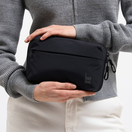 COMMUTER TECH POUCH Tasche in black (Schwarz) von einer Frau in der Hand gehalten.