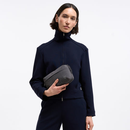 COMMUTER TECH POUCH Tasche in shark (Dunkelgrau) von einer Frau in der Hand gehalten.