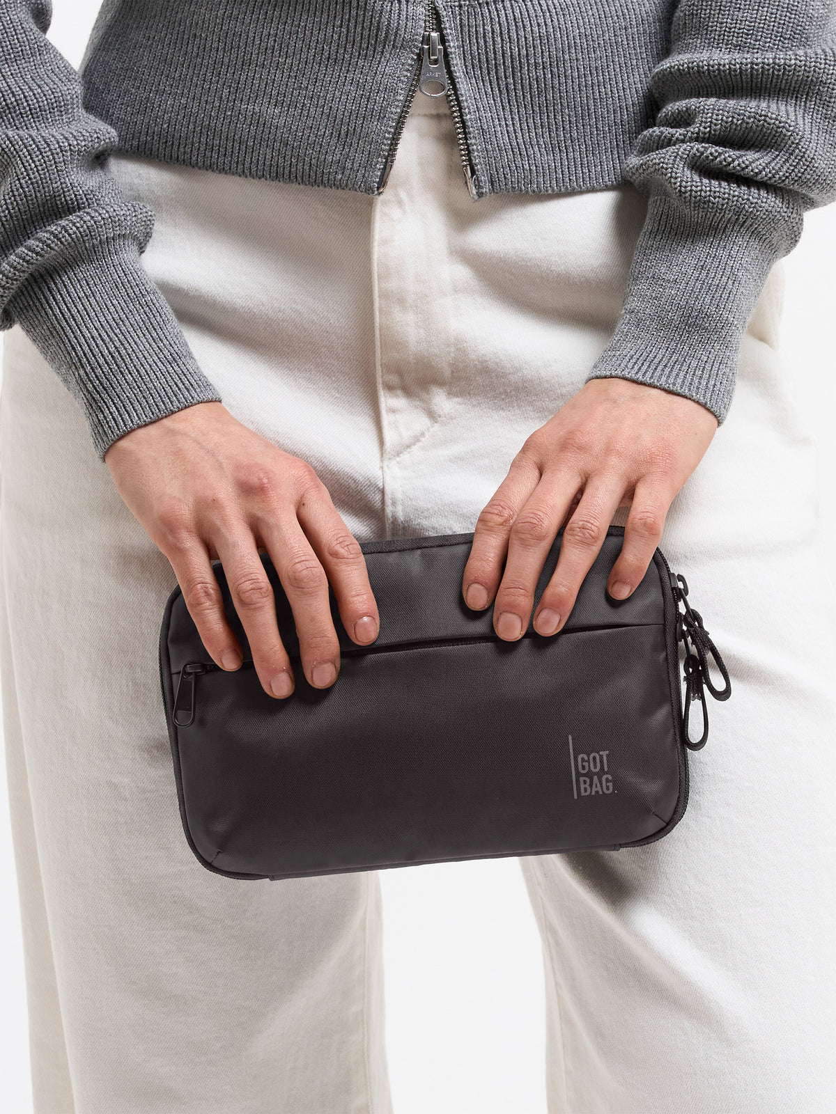 TECH POUCH Tasche in mussel (dunkles Braun-Grau) von einer Frau in der Hand gehalten.
