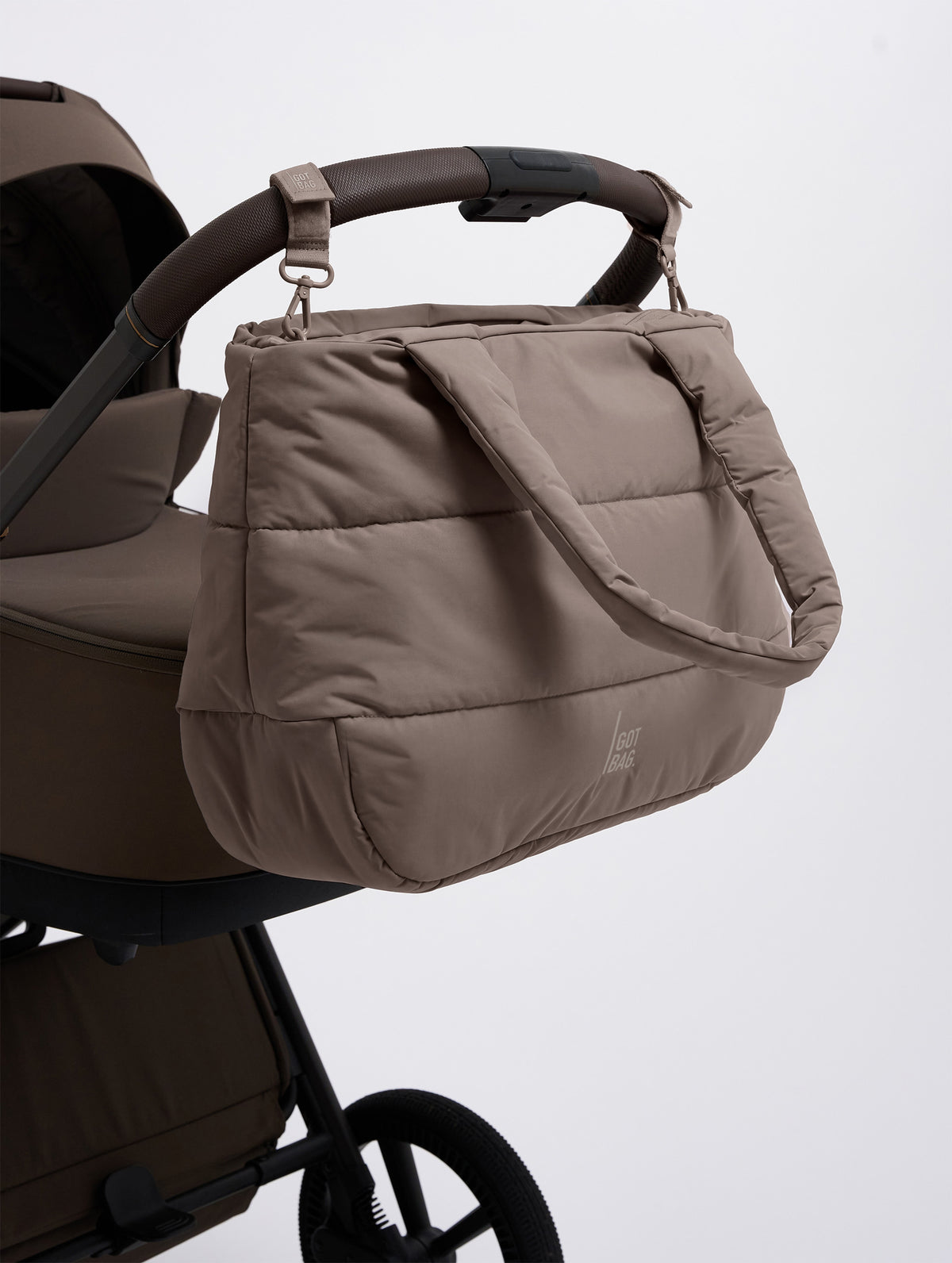 STROLLER STRAP Tasche in oyster (klassisches Taupe-Braun) an einem Kinderwagen hängend.