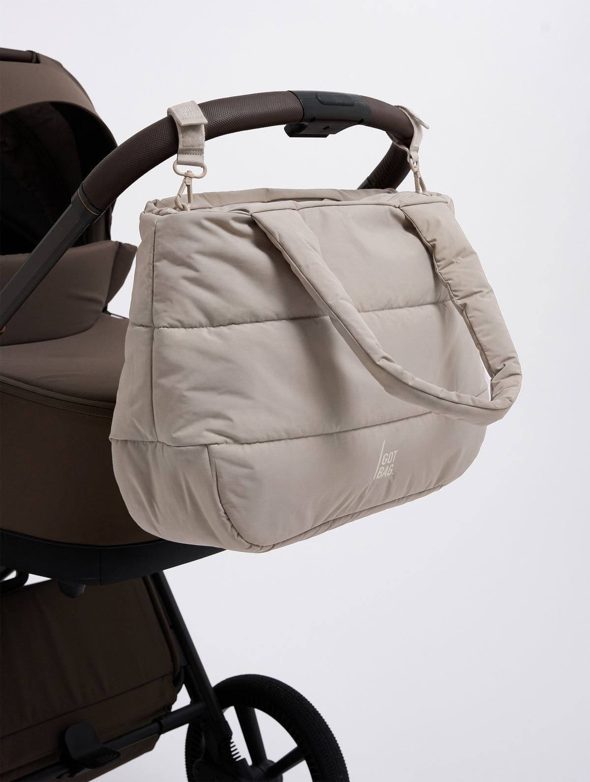STROLLER STRAP Accessoires in scallop (helles Beige) am Kinderwagengriff befestigt.