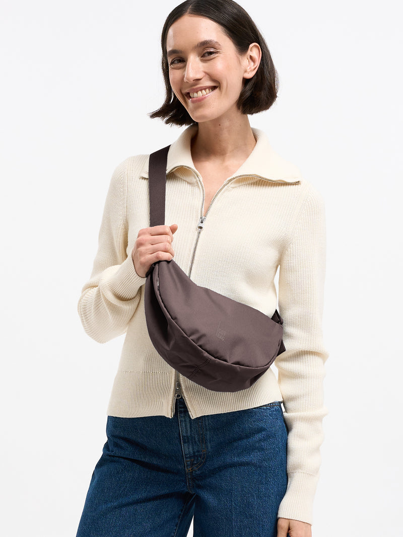 MOON BAG SMALL MONOCHROME Tasche in sea lion (dunkles Schokobraun) von einer Frau crossbody getragen.