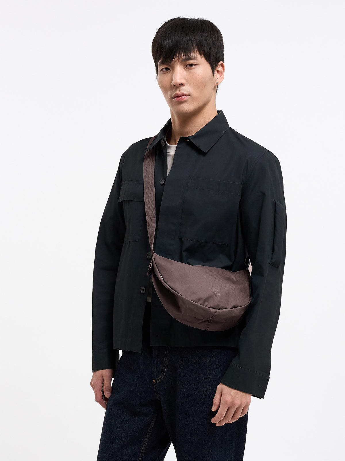 MOON BAG SMALL MONOCHROME Tasche in sea lion (dunkles Schokobraun) von einem Mann crossbody getragen.