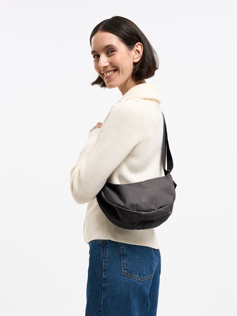 MOON BAG SMALL Tasche in mussel (dunkles Braun-Grau) von einer Frau crossbody getragen.
