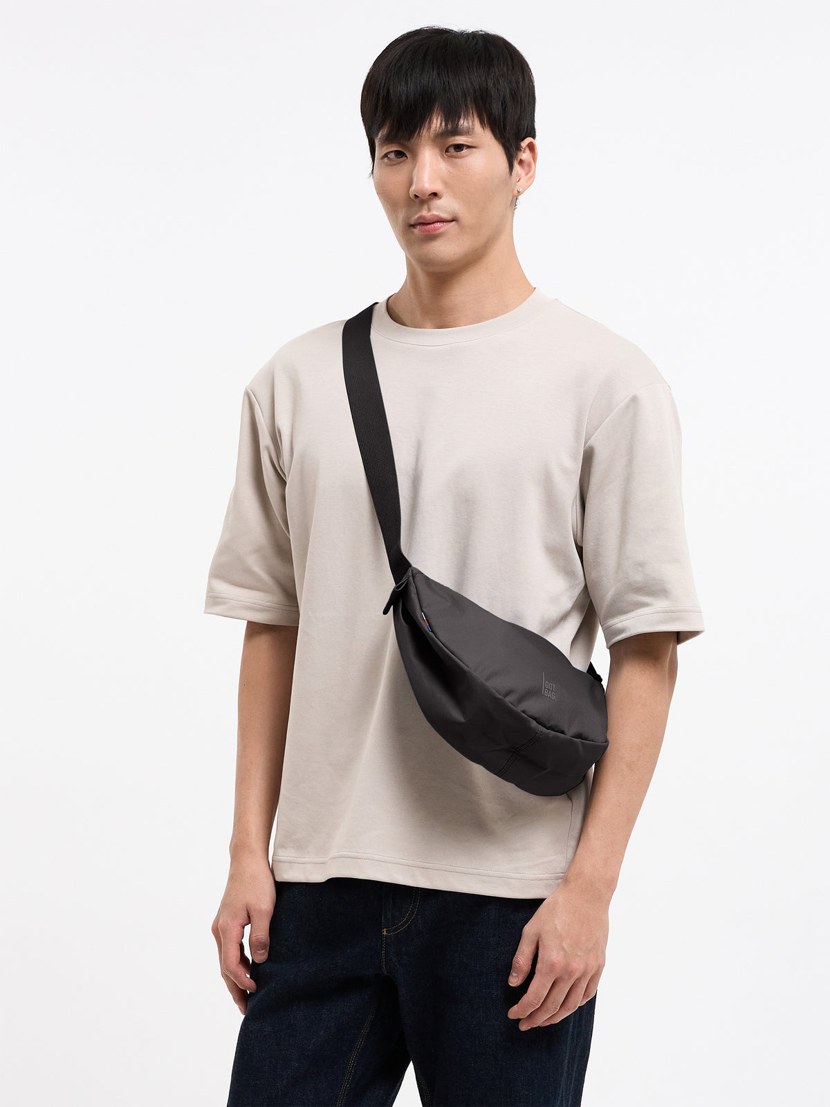 MOON BAG SMALL Tasche in mussel (dunkles Braun-Grau) von einem Mann crossbody getragen.