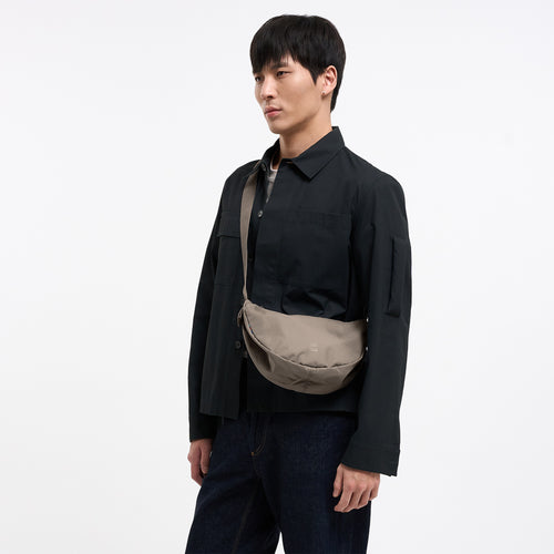 MOON BAG SMALL Tasche in seal (dunkler Beigeton) von einem Mann crossbody getragen.