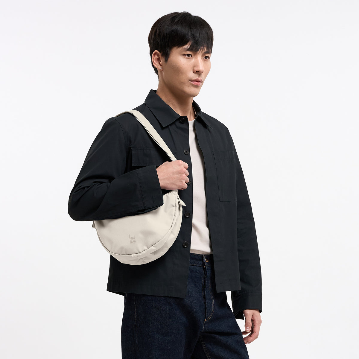 MOON BAG SMALL Tasche in soft shell (warmes Cremeweiß) von einem Mann über der Schulter getragen.