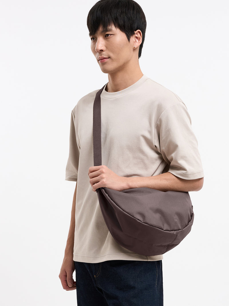 MOON BAG LARGE MONOCHROME Tasche in oyster (klassisches Taupe-Braun) von einem Mann crossbody getragen.