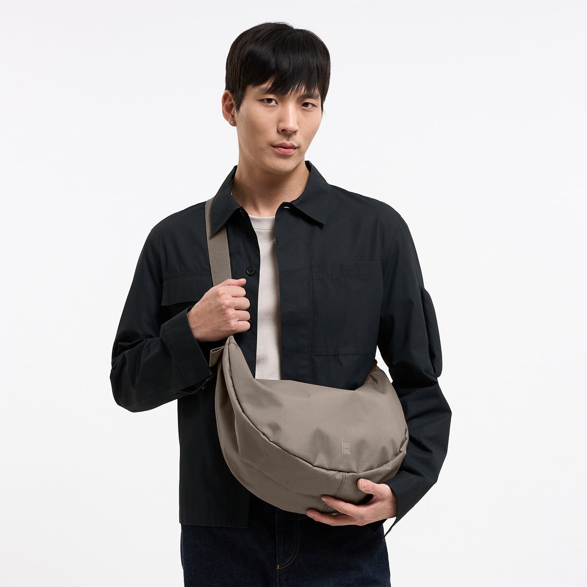 MOON BAG LARGE MONOCHROME Tasche in seal (dunkler Beigeton) von einem Mann crossbody getragen.