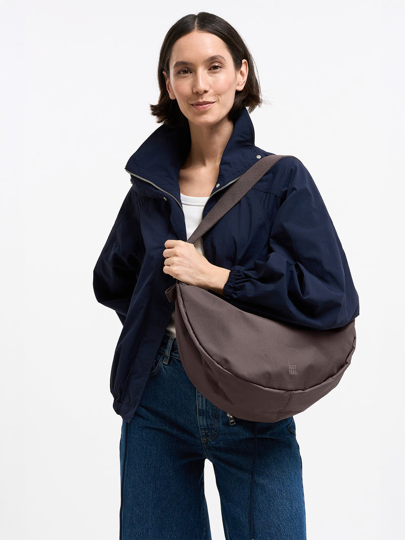 MOON BAG LARGE MONOCHROME Tasche in sea lion (dunkles Schokobraun) von einer Frau crossbody getragen.
