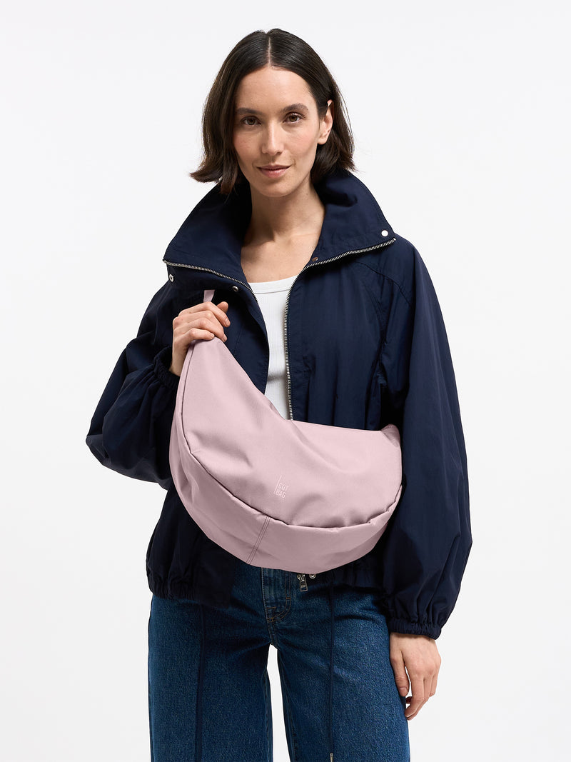 MOON BAG LARGE MONOCHROME Tasche in pink dolphin (blasses Hellrosa) von einer Frau in der Hand gehalten.
