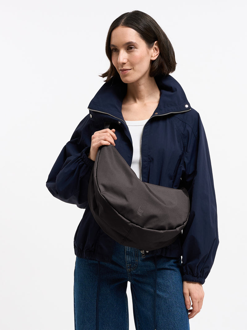 MOON BAG LARGE Tasche in mussel (dunkles Braun-Grau) von einer Frau crossbody getragen.