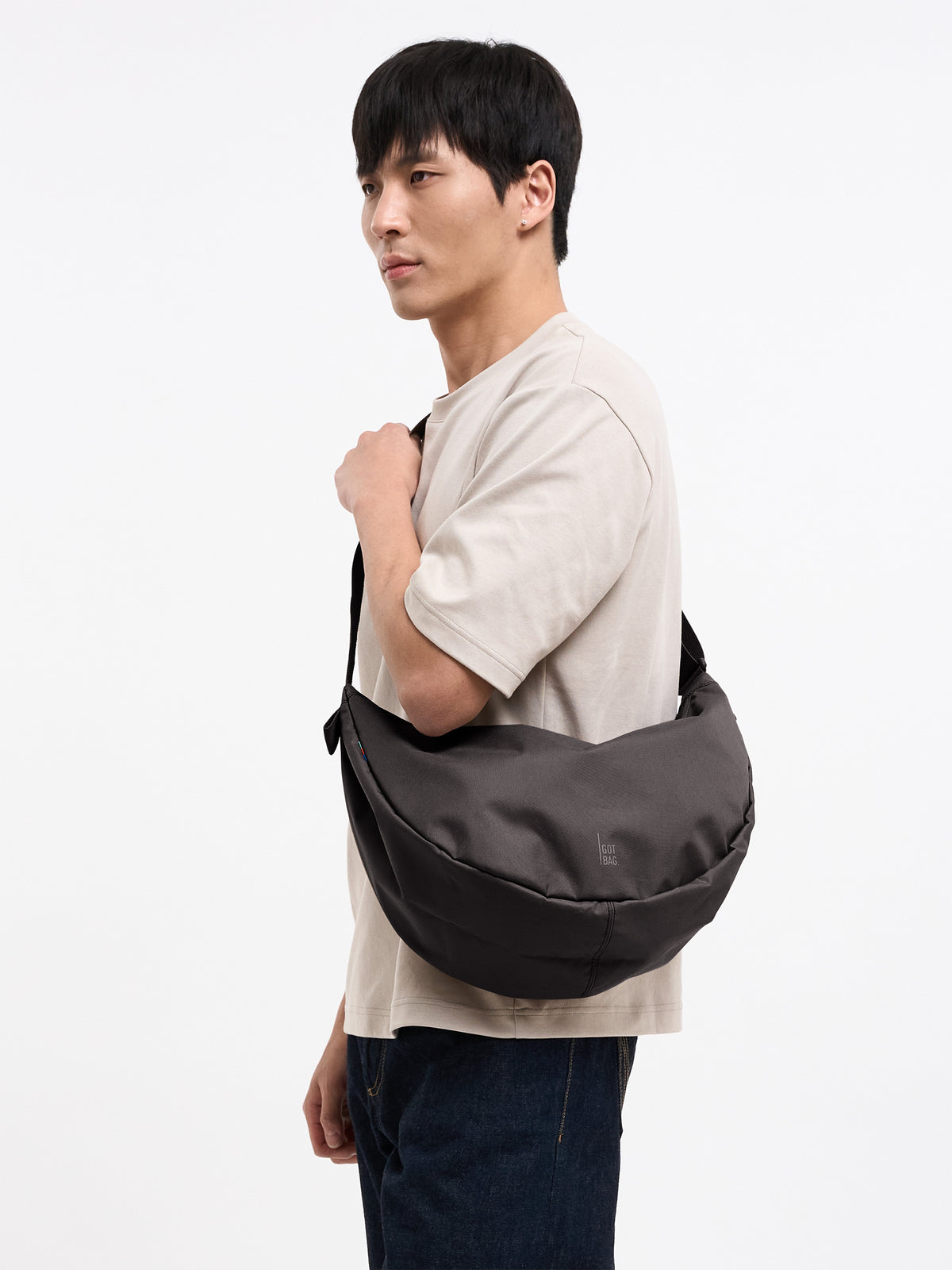 MOON BAG LARGE Tasche in mussel (dunkles Braun-Grau) von einem Mann crossbody getragen.