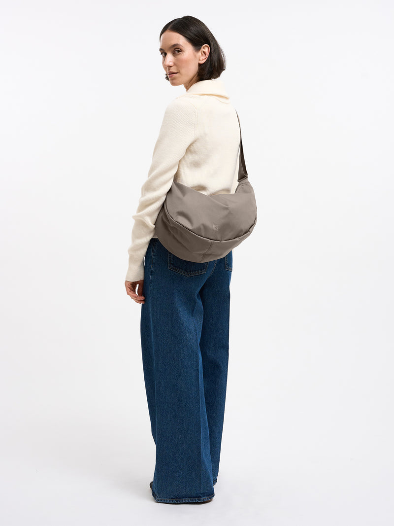MOON BAG LARGE Tasche in seal (dunkler Beigeton) von einer Frau über der Schulter getragen.