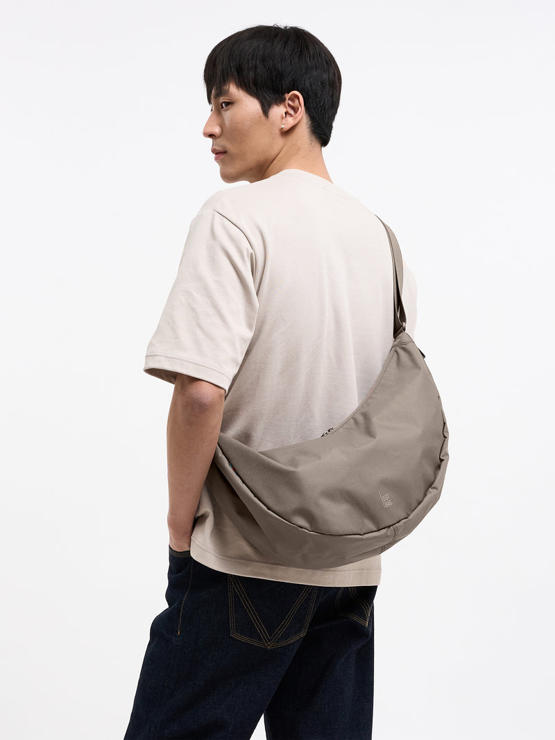 MOON BAG LARGE Tasche in seal (dunkler Beigeton) von einem Mann über der Schulter getragen.