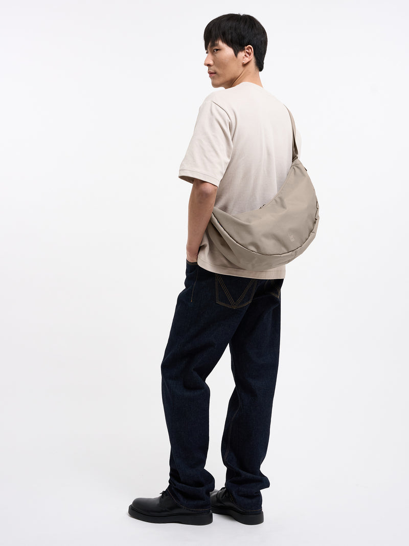 MOON BAG LARGE Tasche in scallop (helles Beige) von einem Mann über der Schulter getragen.