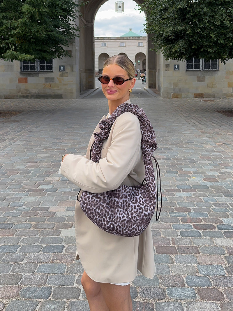 MOON BAG RUFFLE CAT SHARK Tasche in sea lion (dunkles Schokobraun) von einer Frau über der Schulter getragen.
