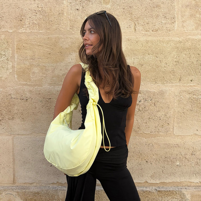 MOON BAG RUFFLE tas in sea lemon (zacht pastelgeel) over de schouder gedragen door een vrouw.