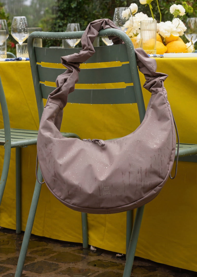 MOON BAG RUFFLE tas in oyster (Klassiek taupe-bruin) hangend aan een stoel met regendruppels.