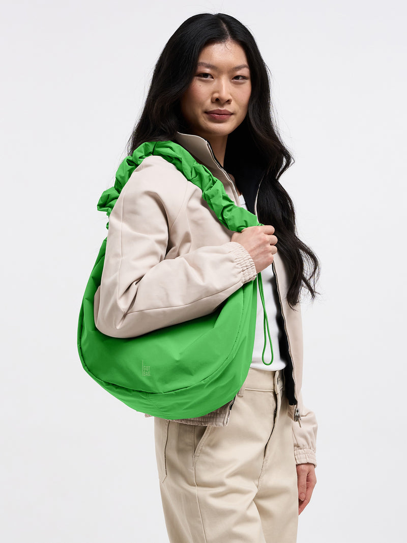 MOON BAG RUFFLE Tasche in leaf von einer Frau über der Schulter getragen.