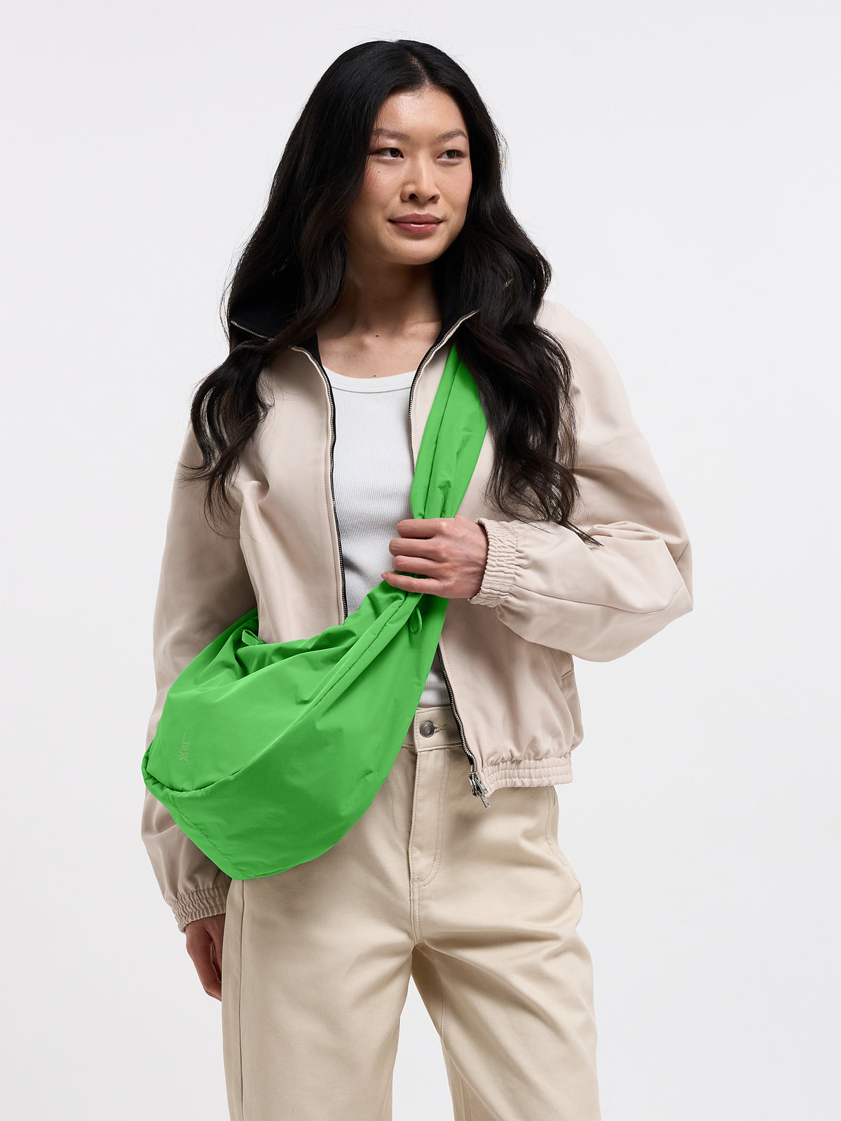 MOON BAG RUFFLE Tasche in leaf, von einer Frau mit langen, dunklen Haaren in beiger Bomberjacke getragen.