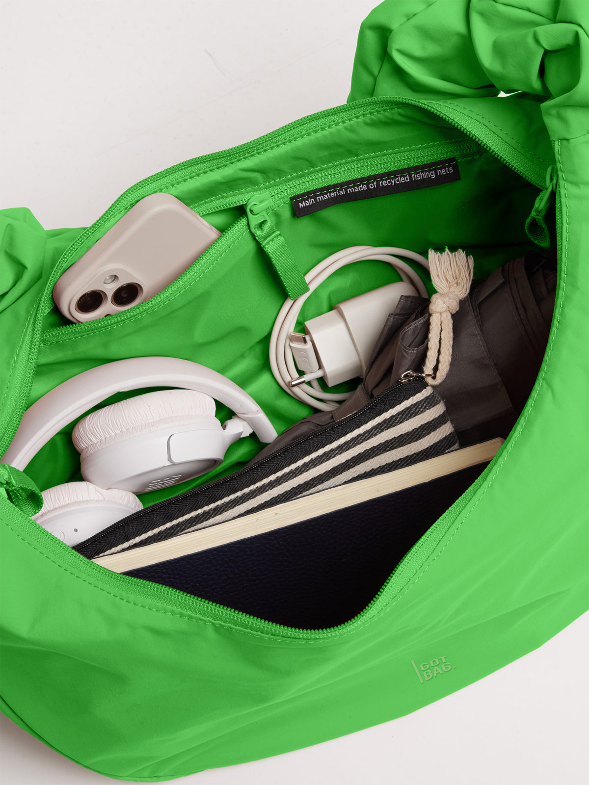 MOON BAG RUFFLE Tasche, Innenansicht gefüllt mit Handy, Kopfhörern, Ladekabel. Materialhinweis aus recycelten Fischernetzen.