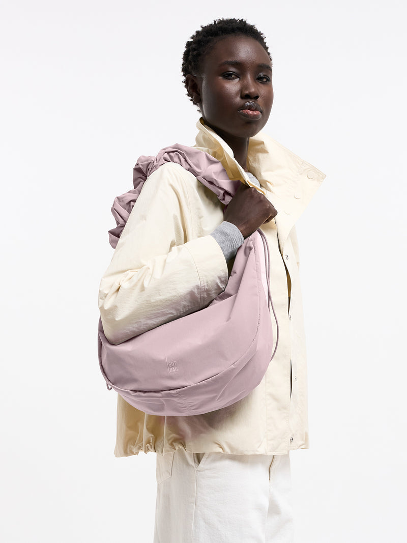 MOON BAG RUFFLE Tasche in pink dolphin (blasses Hellrosa) von einer Frau über der Schulter getragen.