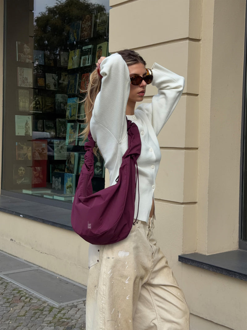 MOON BAG RUFFLE taška v kraken (burgundské) nošená přes rameno ženou.