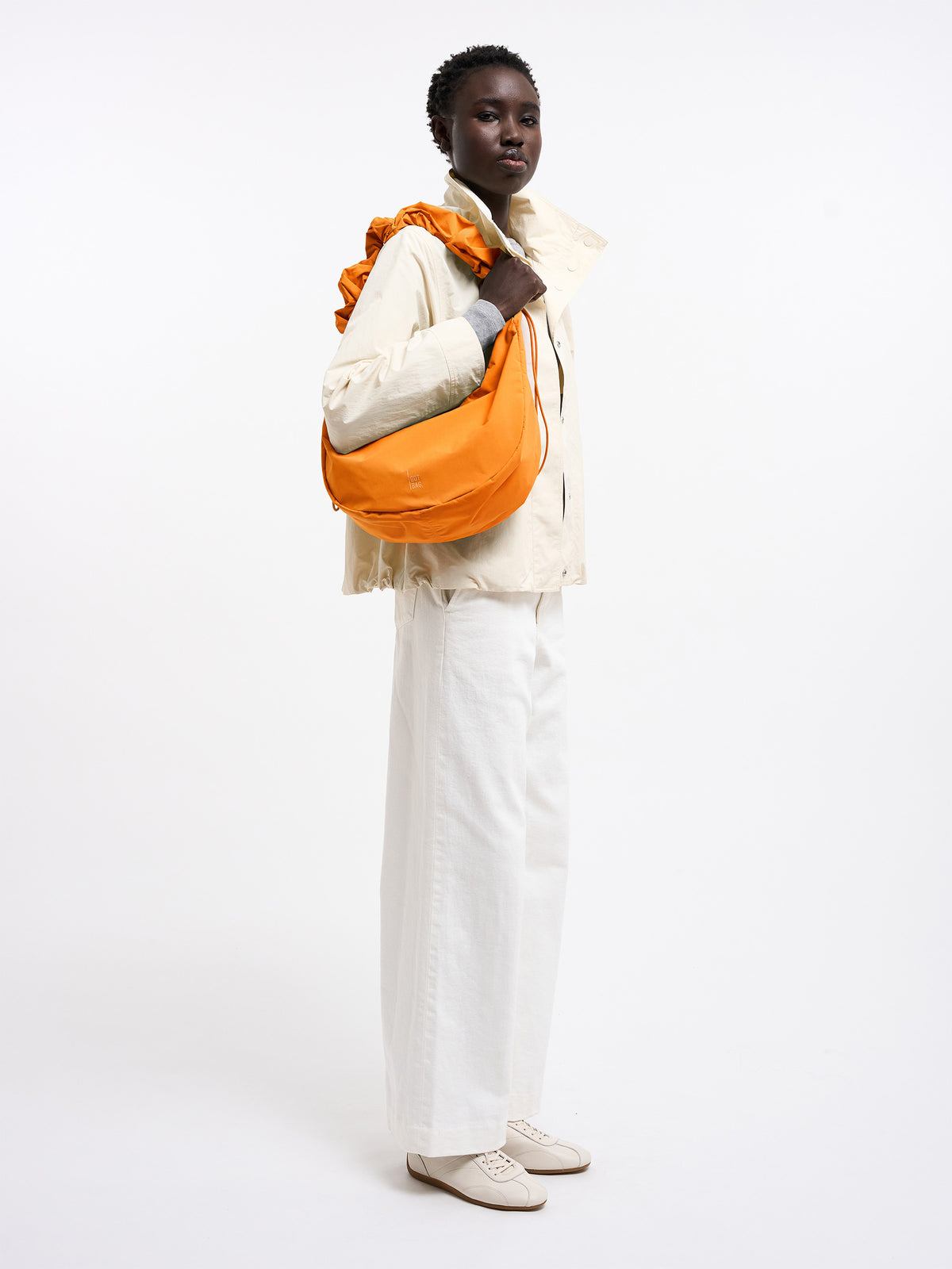 MOON BAG RUFFLE Tasche in clownfish (leuchtendes Orange-Gelb) von einer Frau über der Schulter getragen.