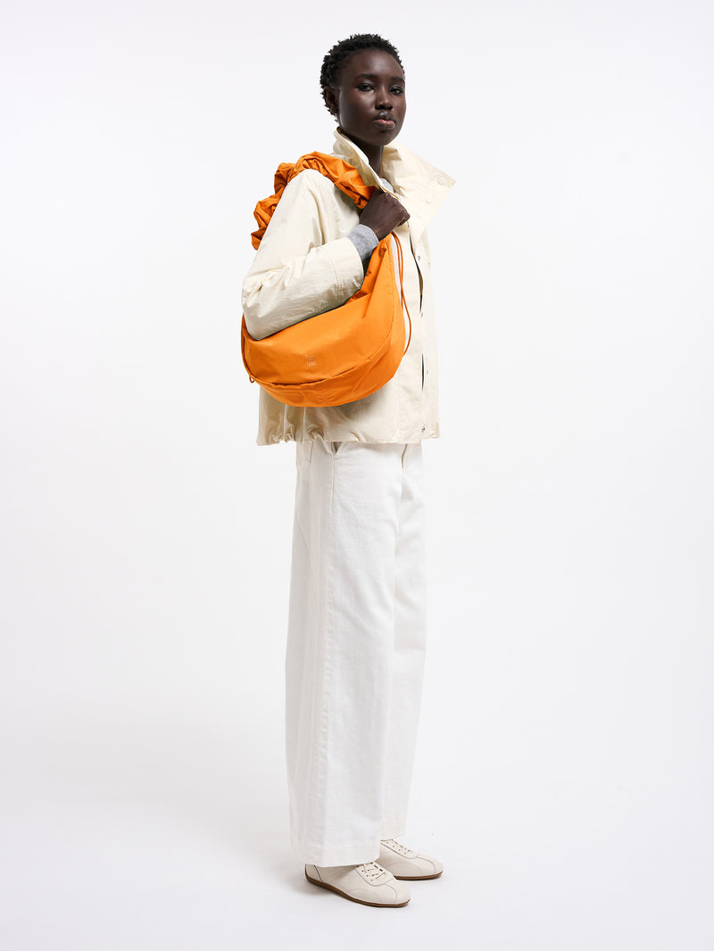 MOON BAG RUFFLE Tasche in clownfish (leuchtendes Orange-Gelb) von einer Frau über der Schulter getragen.