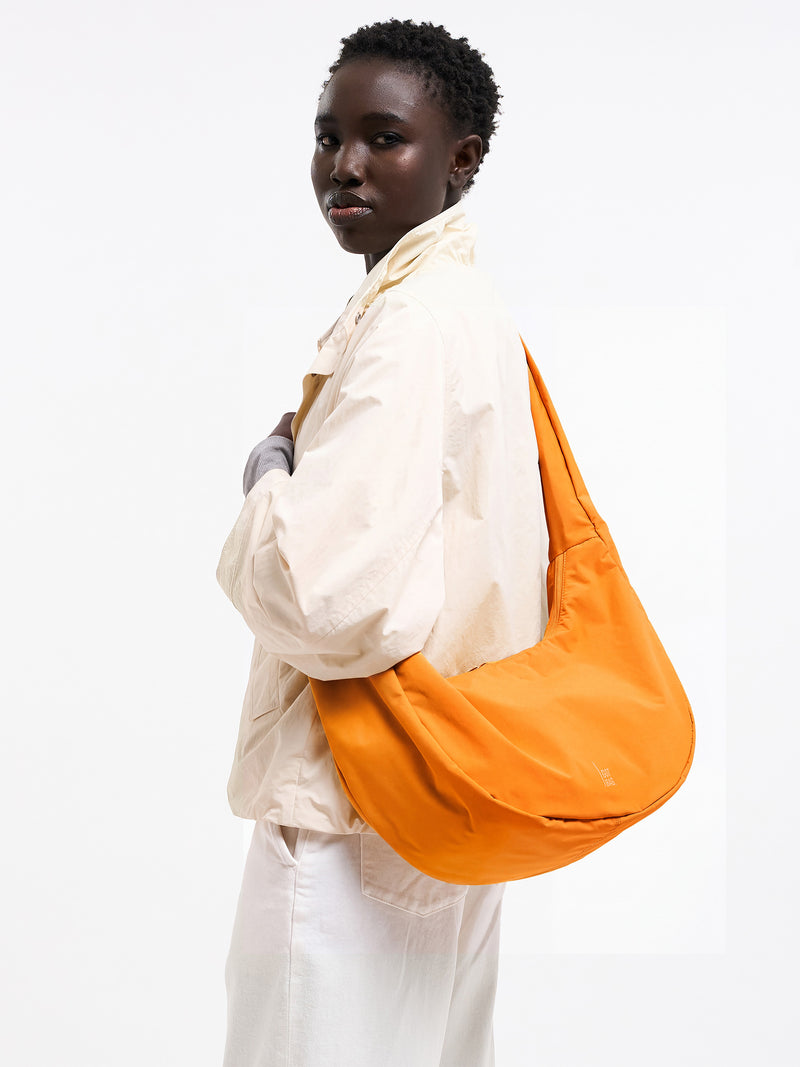 MOON BAG RUFFLE Tasche in clownfish (leuchtendes Orange-Gelb) von einer Frau crossbody getragen.