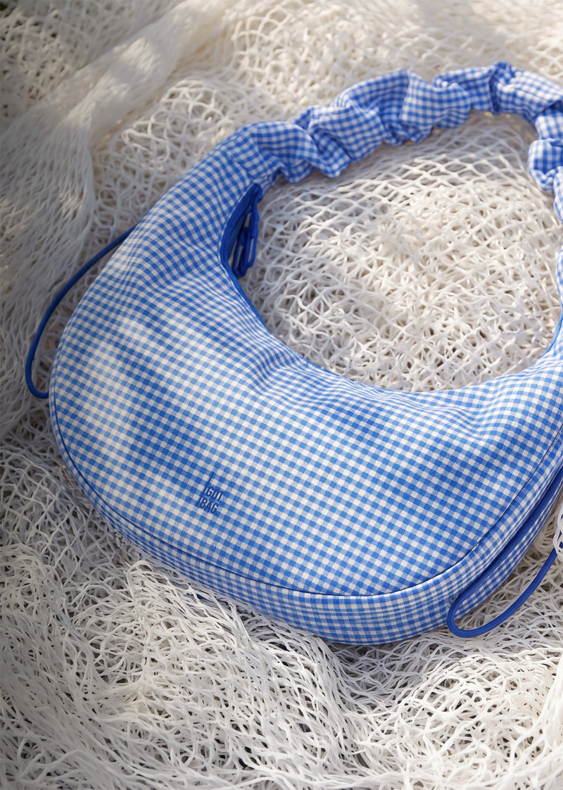 MOON BAG RUFFLE VICHY tas in cobalt (helder kobaltblauw) liggend op een lichte netondergrond.
