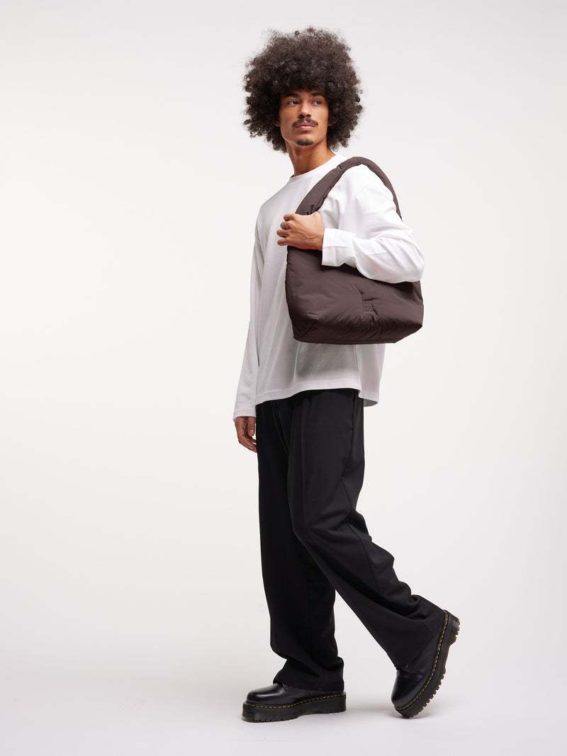 CLOUD SHOULDER BAG Tasche in sea lion (dunkles Schokobraun) von einem Mann über der Schulter getragen.