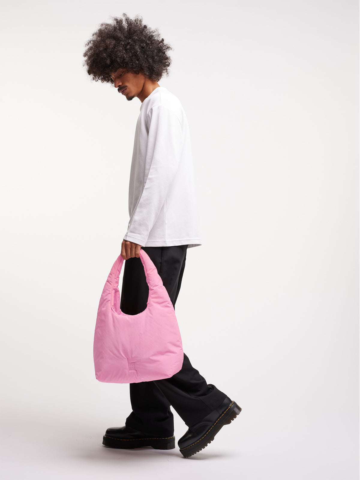 CLOUD SHOULDER BAG Tasche in sea rose (sattes Pastell-Rosa) von einem Mann in der Hand gehalten.