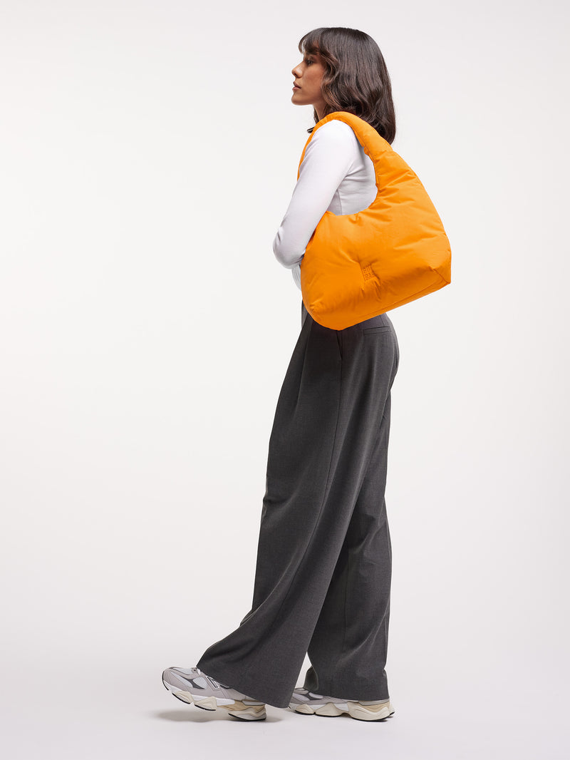CLOUD SHOULDER BAG Tasche in clownfish (leuchtendes Orange-Gelb) von einer Frau über der Schulter getragen.