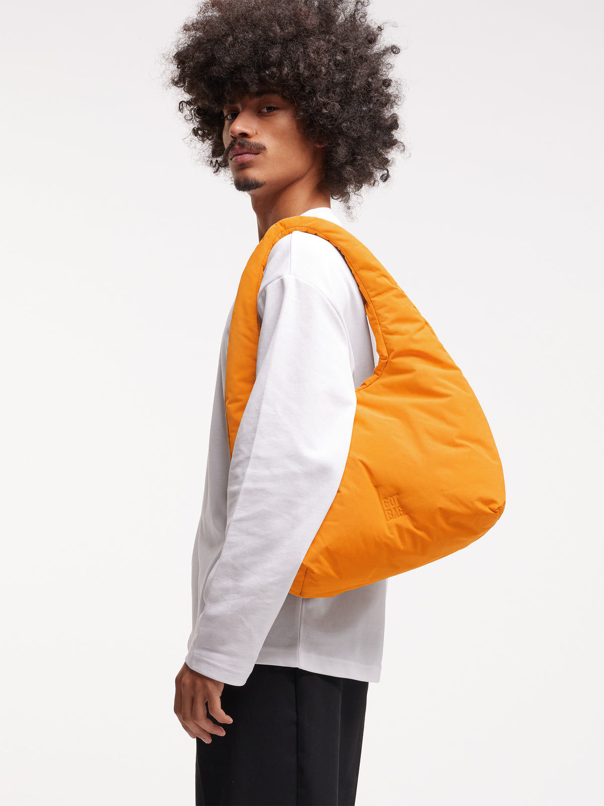 CLOUD SHOULDER BAG Tasche in clownfish (leuchtendes Orange-Gelb) von einem Mann über der Schulter getragen.
