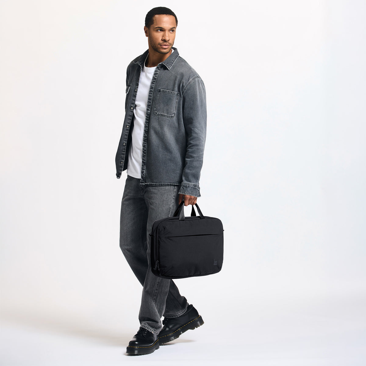 COMMUTER BAG Tasche in black (Schwarz) von einem Mann in der Hand gehalten.