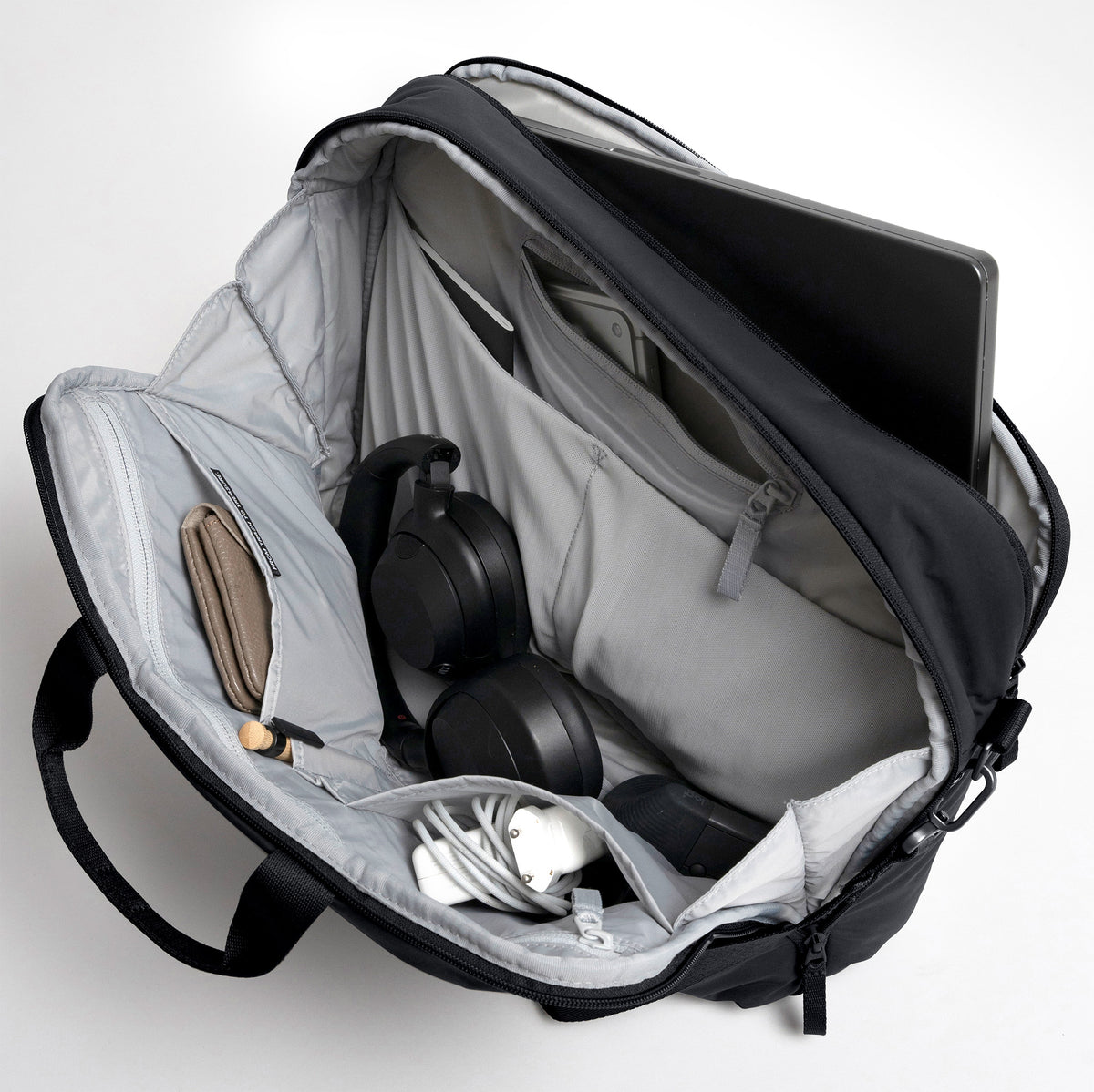 COMMUTER BAG Tasche in black (Schwarz), offene Innenansicht mit Laptop, Kopfhörern, Geldbörse und Zubehör.