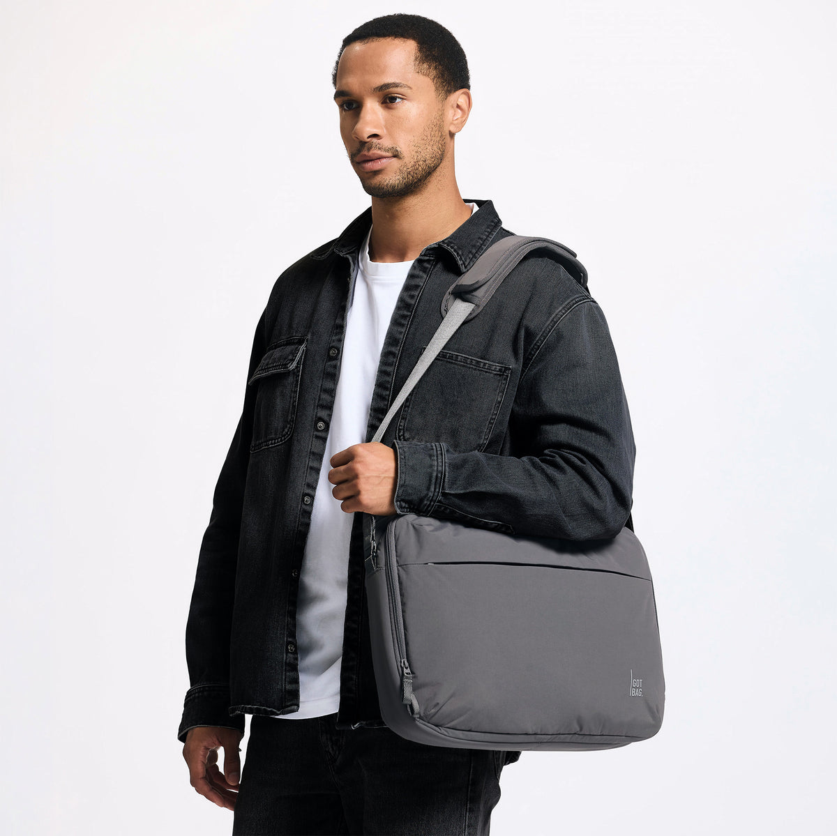 COMMUTER BAG Tasche in shark (Dunkelgrau) von einem Mann über der Schulter getragen.