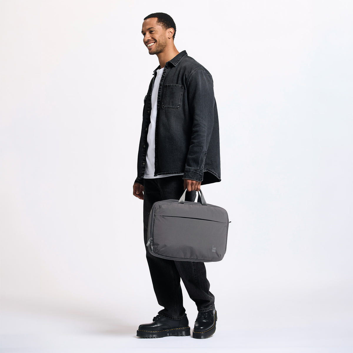 COMMUTER BAG Tasche in shark (Dunkelgrau) von einem Mann in der Hand gehalten.