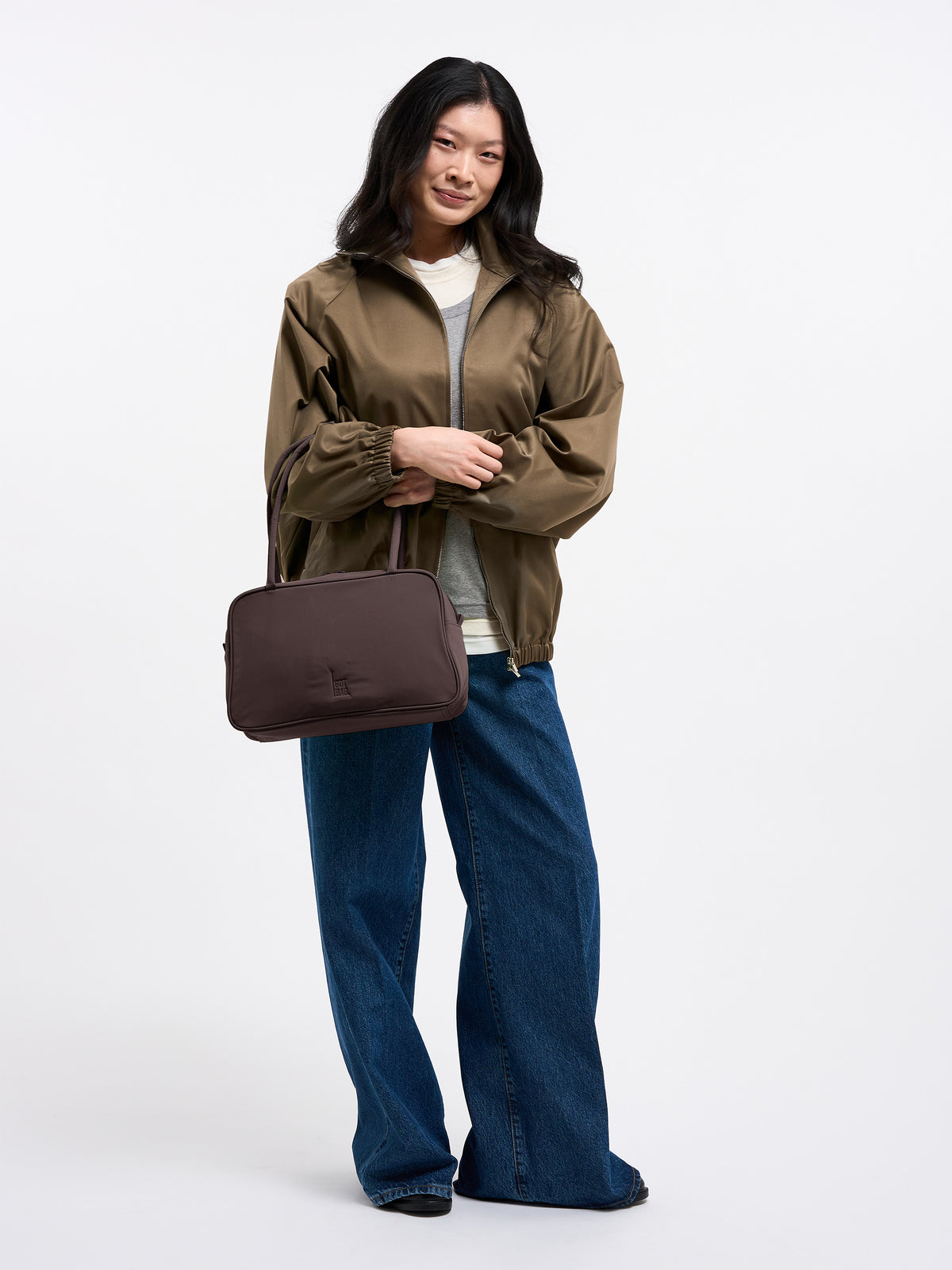 STRIKE BAG Tasche in sea lion (dunkles Schokobraun) von einer Frau in der Hand gehalten.
