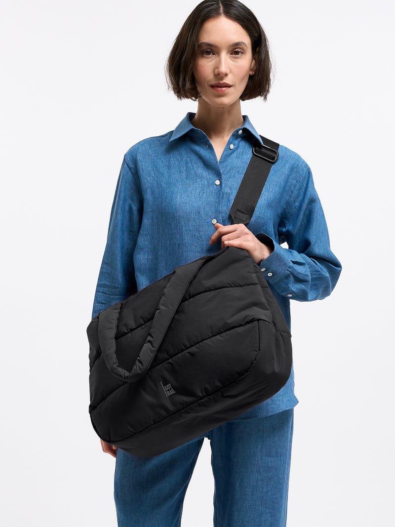 PUFFER HORIZON TOTE BAG Tasche in black (Schwarz) von einer Frau über der Schulter getragen.