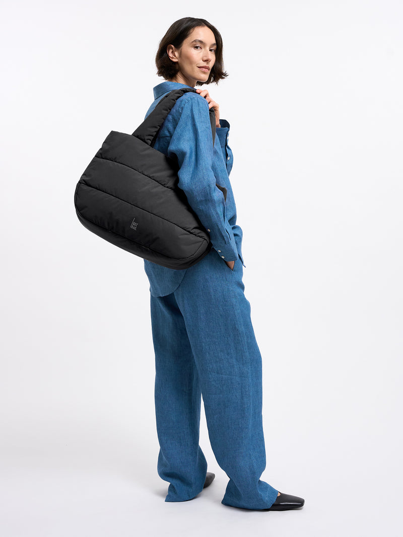 PUFFER HORIZON TOTE BAG Tasche in black (Schwarz) von einer Frau über der Schulter getragen.
