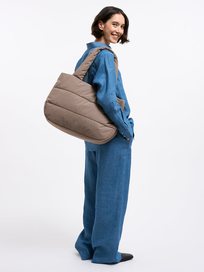 PUFFER HORIZON TOTE BAG Tasche in oyster (klassisches Taupe-Braun) von einer Frau über der Schulter getragen.