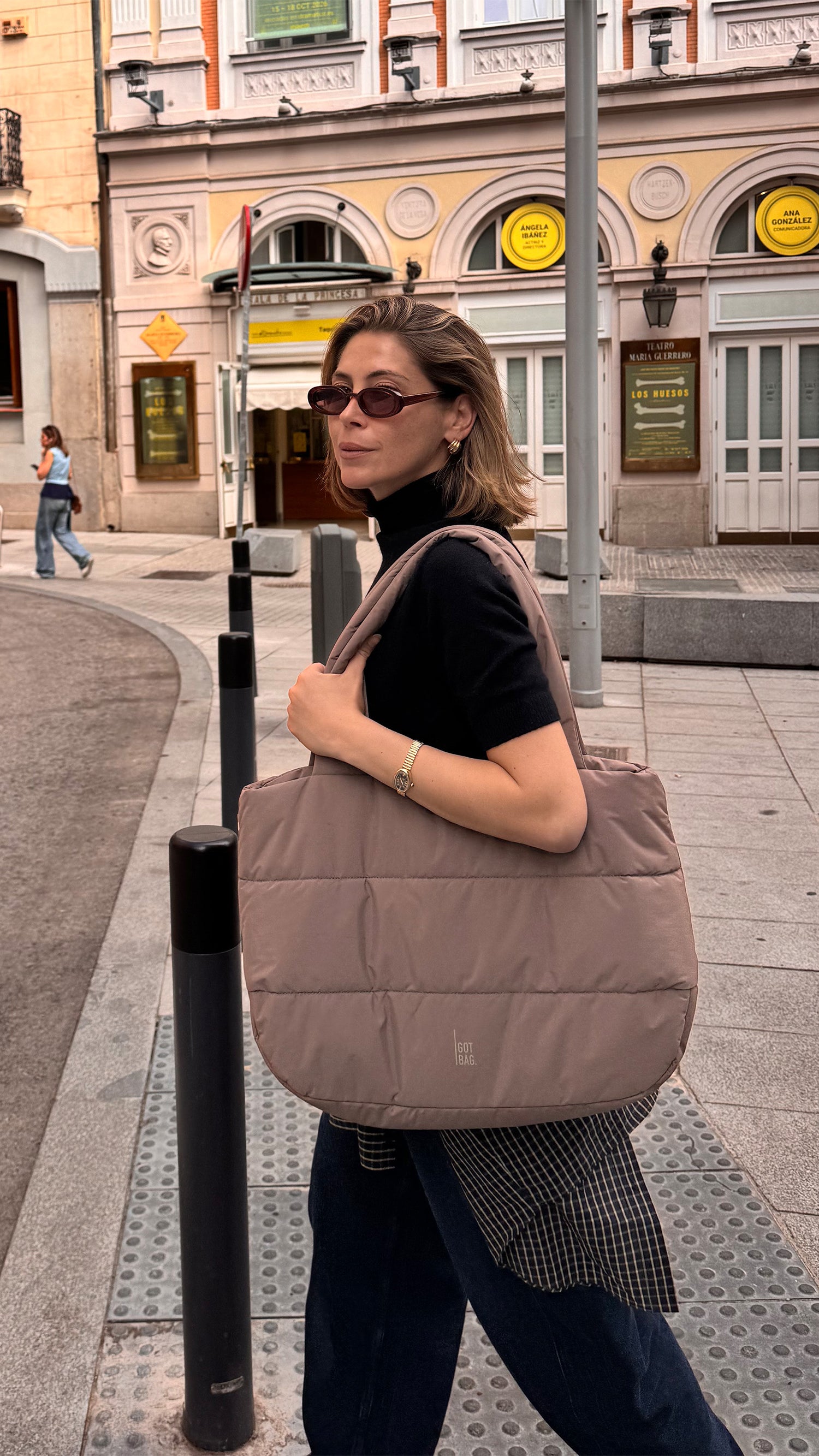 PUFFER HORIZON TOTE BAG tas in oyster (Klassiek taupe-bruin) door een vrouw over de schouder gedragen.