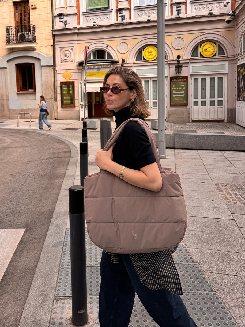 PUFFER HORIZON TOTE BAG tas in oyster (Klassiek taupe-bruin) door een vrouw over de schouder gedragen.