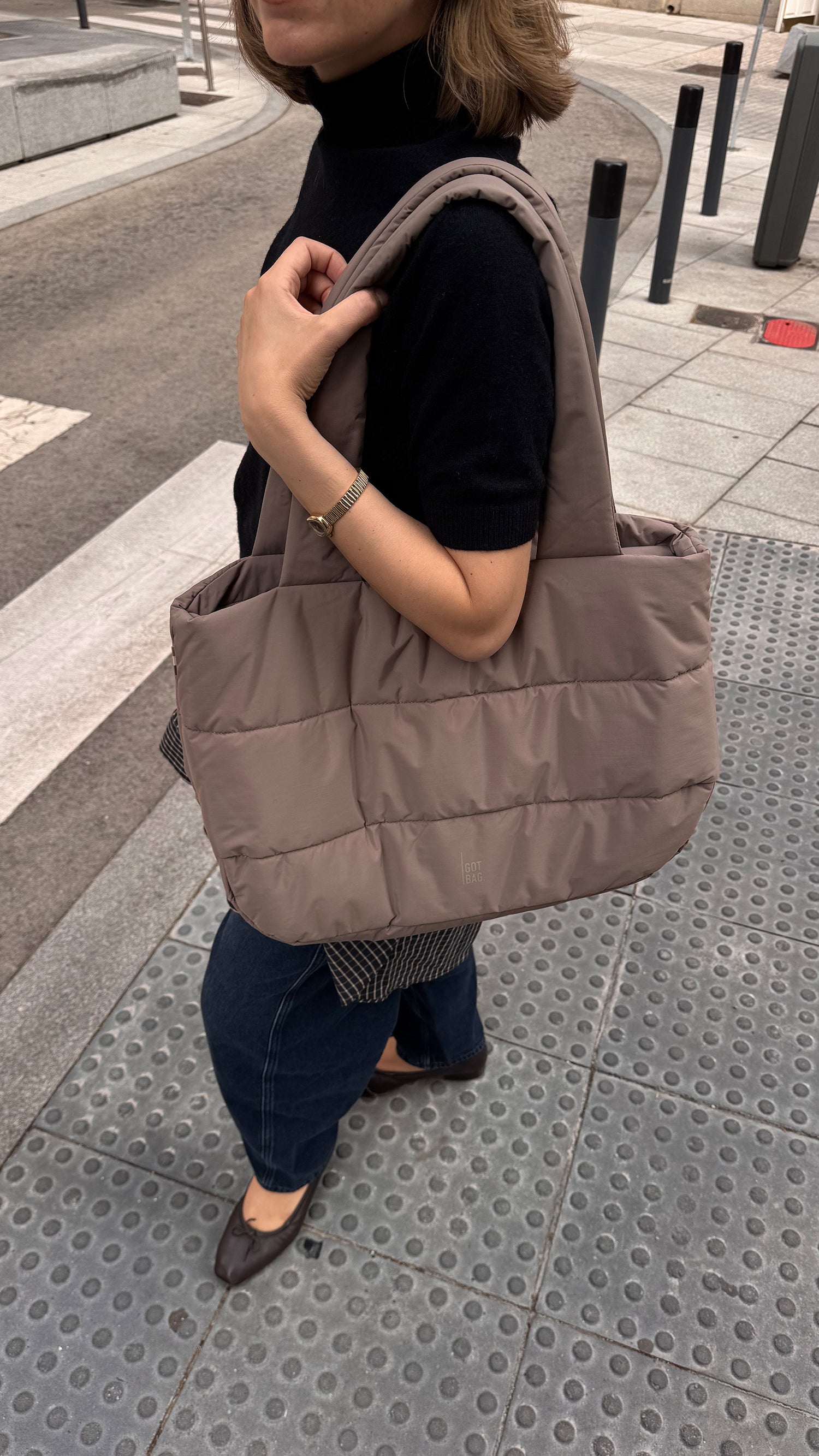PUFFER HORIZON TOTE BAG Tas in oyster (Klassiek taupe-bruin) door een vrouw in de hand gehouden.