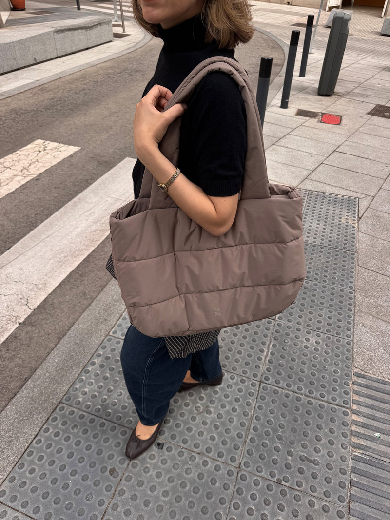 PUFFER HORIZON TOTE BAG Tas in oyster (Klassiek taupe-bruin) door een vrouw in de hand gehouden.
