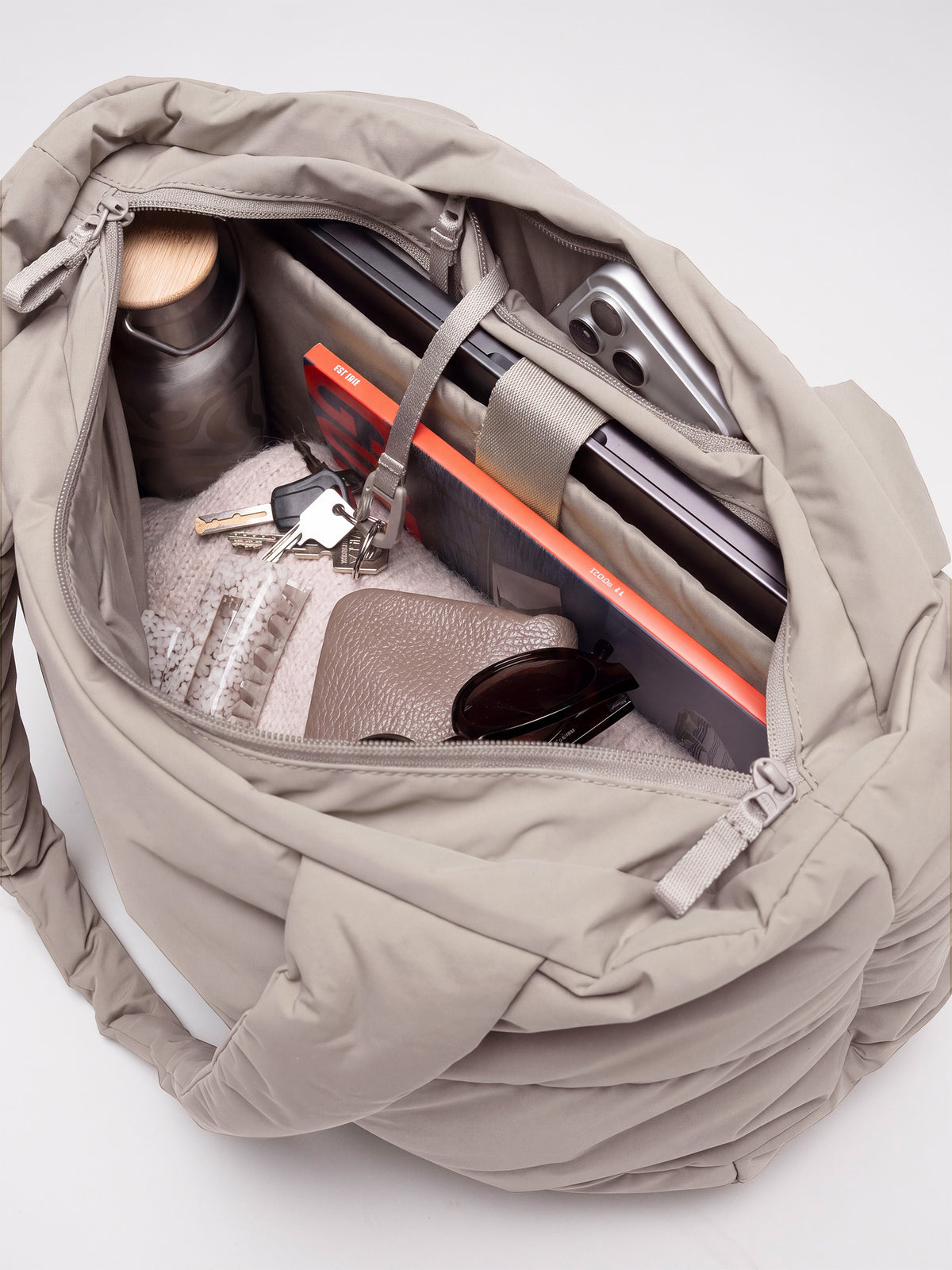 PUFFER HORIZON TOTE BAG Tasche in scallop (helles Beige), offen mit Laptop, Smartphone, Wasserflasche und Schlüsseln gefüllt.